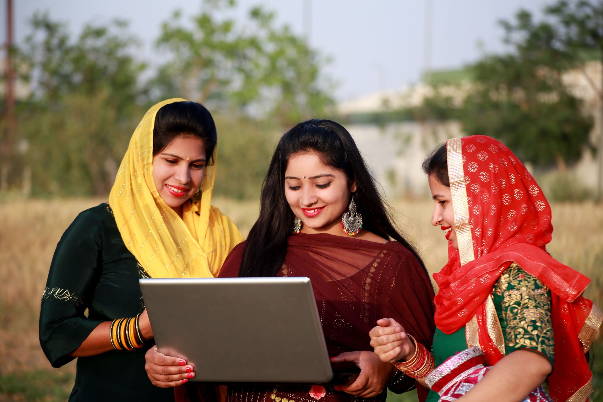 Three rural women using laptop together outdoors in field